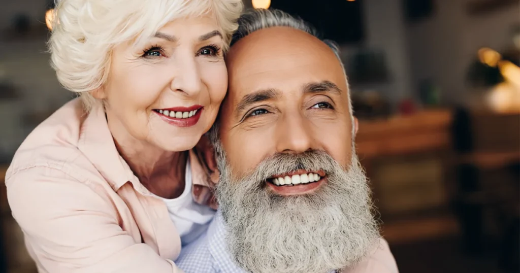 En ældre mand og kvinde, der krammer hinanden og viser deres deres smukke smil med tilpassede tandproteser.